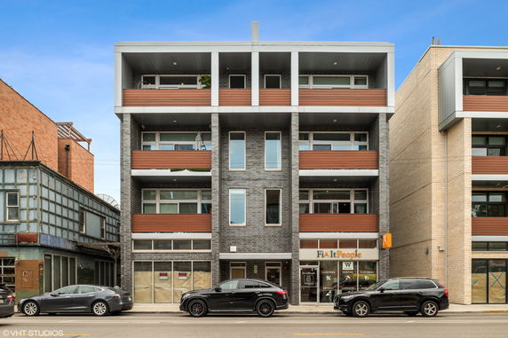 Front view of a modern multi-story building with balconies and shops on the ground level.