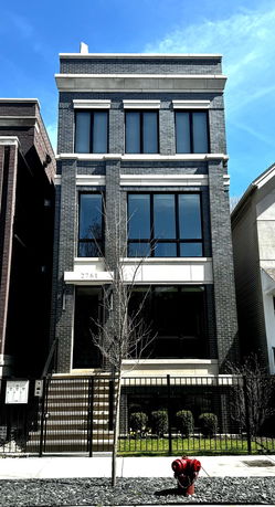Front view of a multi-story brick building with large windows and gated entrance.