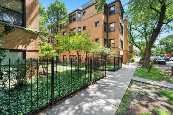 Front view of a multi-story brick building with a sidewalk and iron fence.
