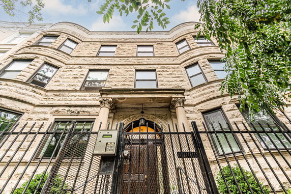 Front view of a multi-story stone building with an ornate entrance and fenced gate.