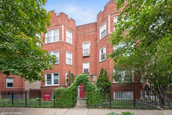 Front view of a multi-story red brick building with a gated entrance.