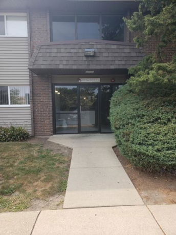 Front view of a building entrance with a glass door and trimmed shrubs.