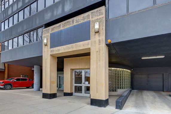 Front view of a modern multi-story building entrance with glass doors and a sheltered driveway.