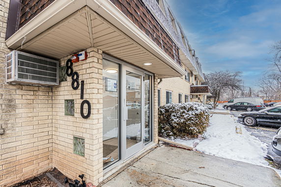 Front view of a brick apartment building with glass doors and an air conditioning unit.
