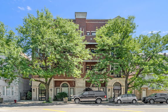 Front view of a multi-story brick building with multiple windows and trees in front.