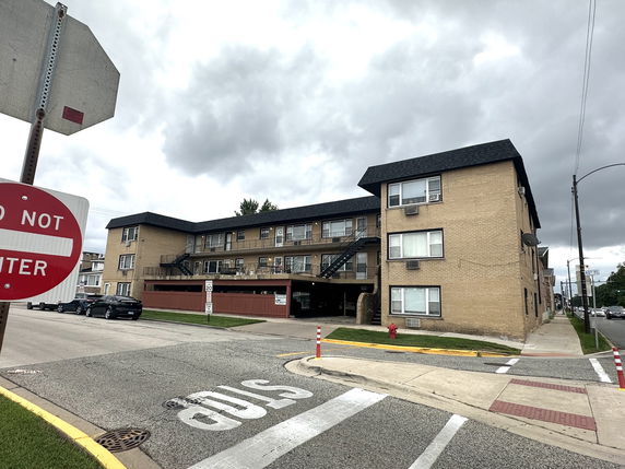 Front view of a three-story apartment building with a parking area and exterior staircases.