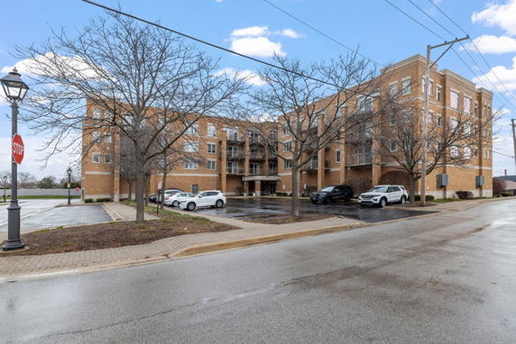 Front view of a multi-story brick apartment building with parking spaces and a few trees in front.