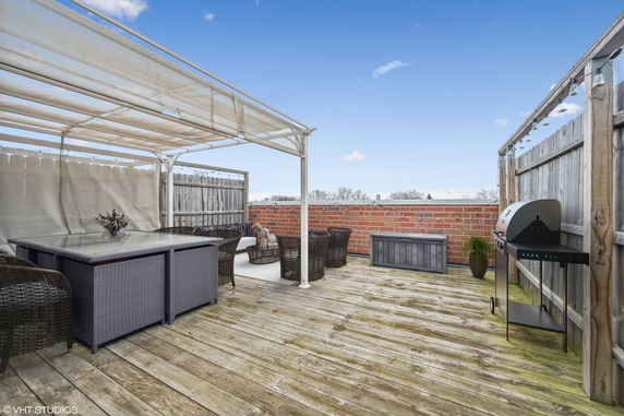 Rooftop area with wooden decking and seating arrangement, covered by a pergola with a barbecue grill nearby.