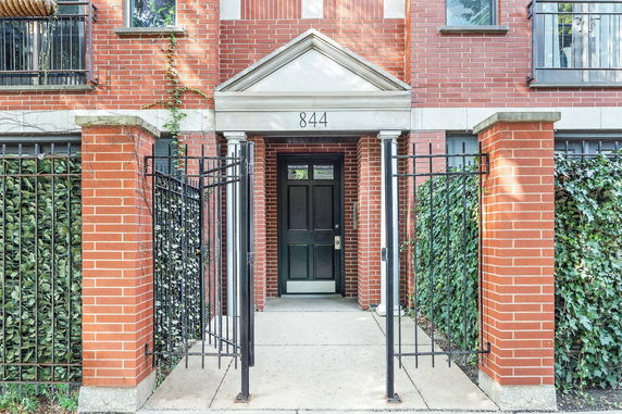 Front view of a brick facade entrance with a black door and gate.