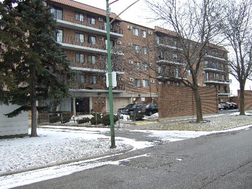 Front view of a multi-story apartment building with balconies and parking area.