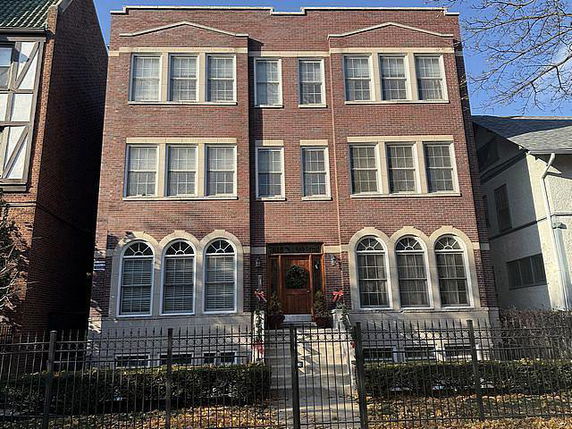 Front view of a three-story brick building with multiple windows and an entrance with steps.