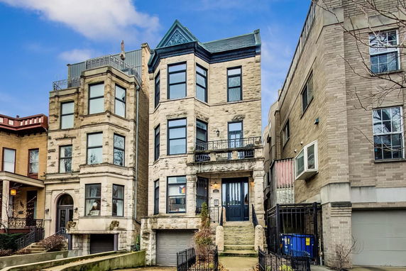 Front view of a three-story stone house with a garage and balcony.