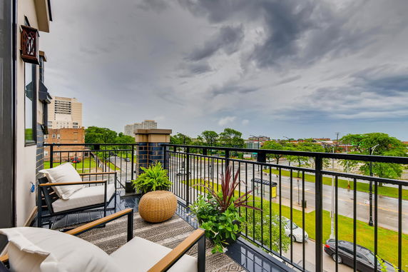 Balcony with outdoor seating overlooking a city street with buildings and trees.