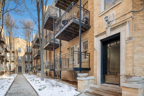Front view of a brick apartment building with multiple balconies and a central entrance.