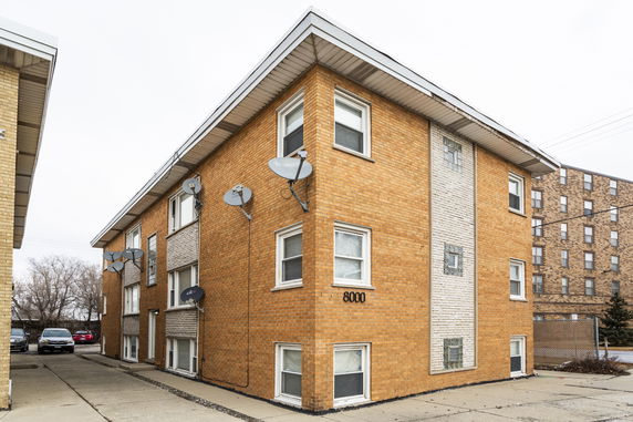 Front view of a multi-story brick apartment building with satellite dishes.