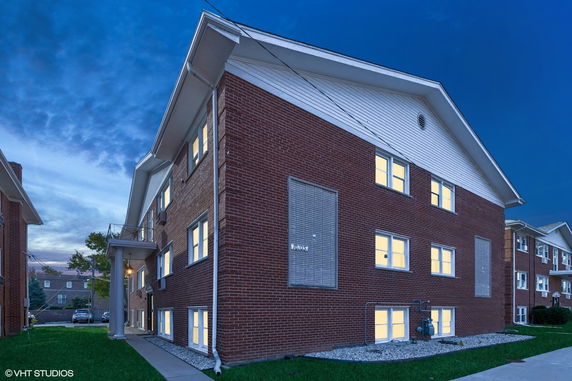 Front view of a multi-story brick apartment building with illuminated windows.