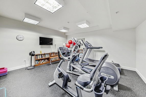 Indoor gym area with exercise equipment and a wall-mounted TV.