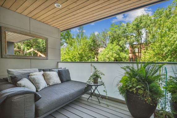 Balcony area with a couch and plants, overlooking trees and houses.