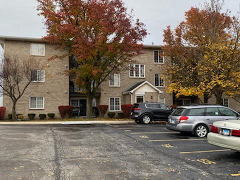 Front view of a three-story brick apartment building with parking area in front.