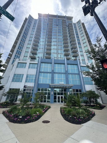 Front view of a tall apartment building with multiple balconies and a landscaped entrance.