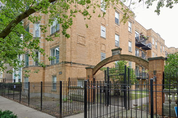 Front view of a multi-story brick building with balconies and a gated entrance.