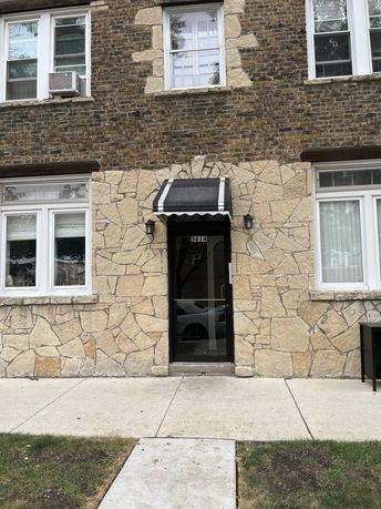 Front view of a building with a stone and brick exterior, including windows and a door with an awning.