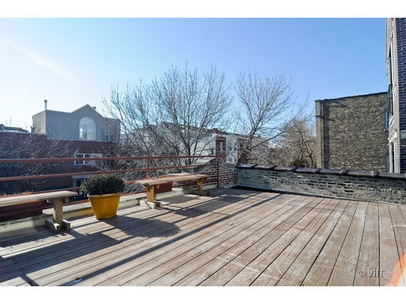 Rooftop terrace with wooden decking and benches, surrounded by railings and adjacent buildings visible.