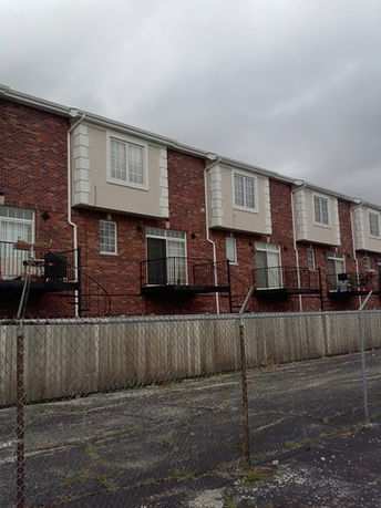 Front view of a row of multi-story townhouses with brick exterior and small balconies.