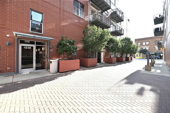 Front view of a building entrance with red brick facade and metal balconies.