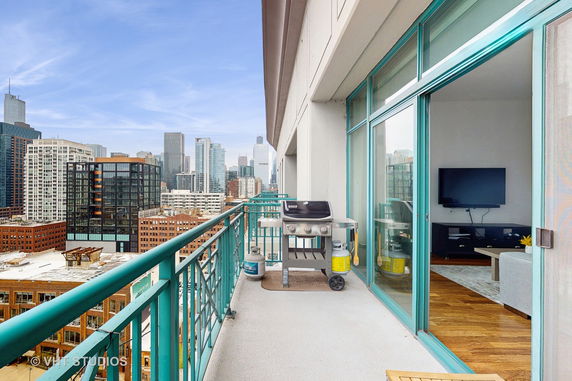 Cityscape view from a balcony with a grill and sliding glass doors leading to an indoor living area.