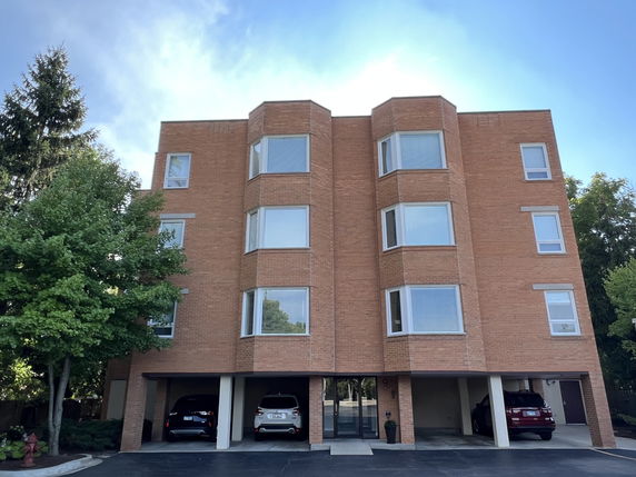 Front view of a four-story brick apartment building with covered parking spaces.