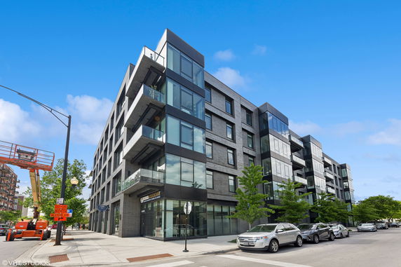 Front view of a modern multi-story apartment building with balconies and large glass windows.
