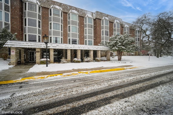 Front view of a multi-story building with large windows and a covered entrance during snowy weather.