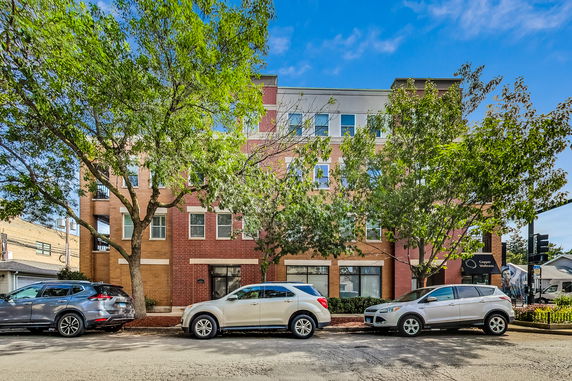 Front view of a multi-story brick building with several windows and trees in front.