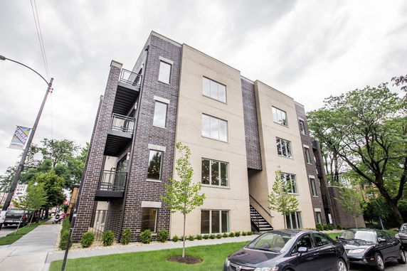 Front view of a multi-story apartment building with large windows and brick facade.