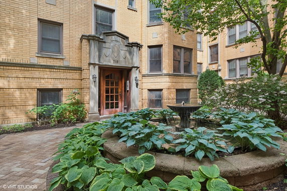 Front view of a brick apartment building with a garden and fountain.