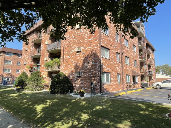 Front view of a four-story brick apartment building with balconies.