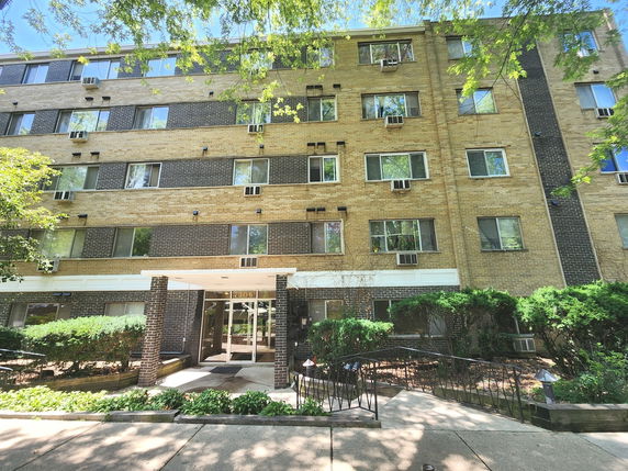 Front view of a multi-story apartment building with multiple windows and air conditioning units.