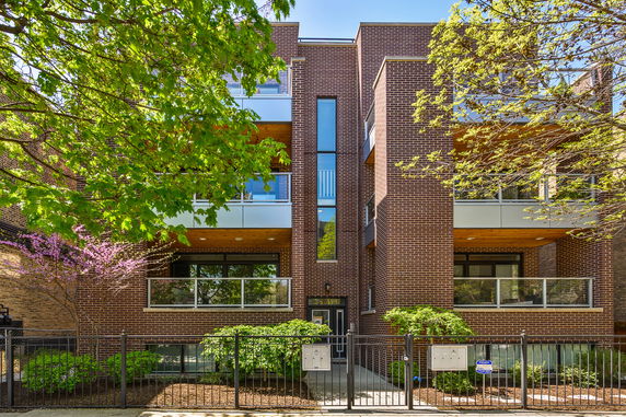 Front view of a modern multi-story brick building with balconies and a gated entrance.