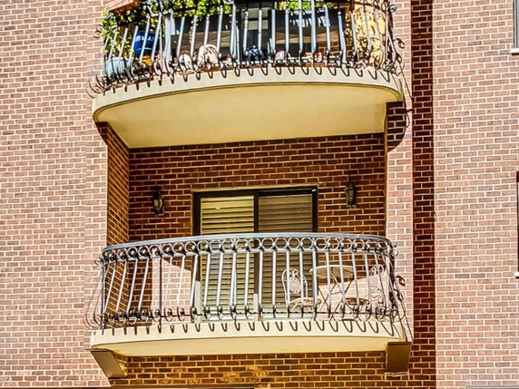Front view of a building with brick facade featuring two balconies with decorative railings.