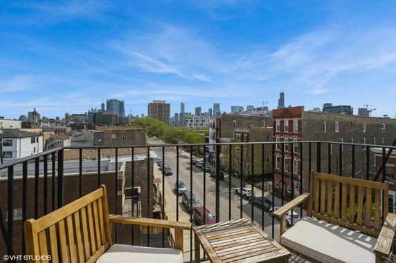 View of urban cityscape from a rooftop patio with wooden seating.