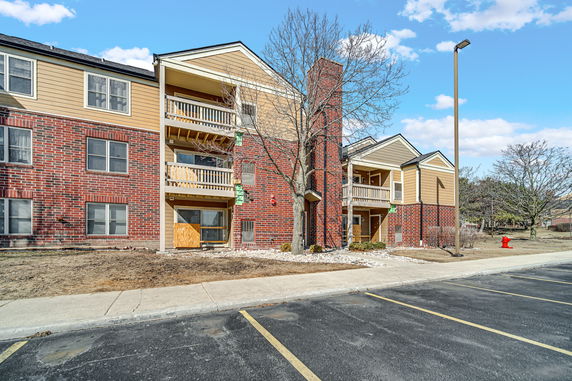 Front view of a multi-story residential building with balconies and a mix of brick and wood siding.