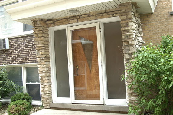 Front view of a building entrance with a glass door and stone pillars.