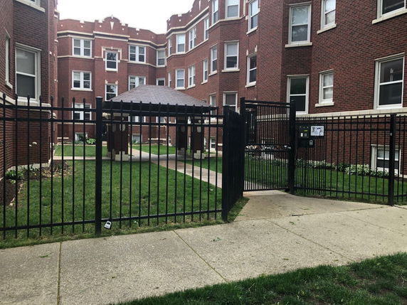 Front view of a multi-story brick apartment building with a gated entrance.