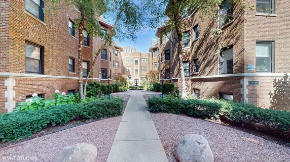 Front view of a multi-story apartment building with brick exterior and landscaped walkway.