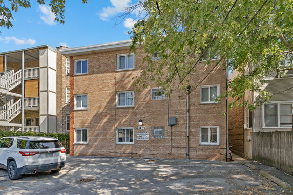 Front view of a brick apartment building with multiple windows and an adjacent parking area.