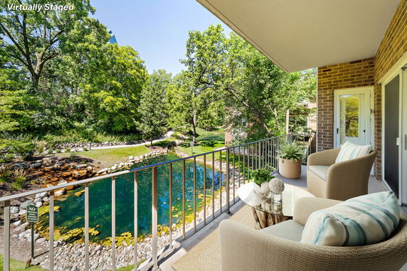 Balcony with seating overlooking a pond and lush greenery.