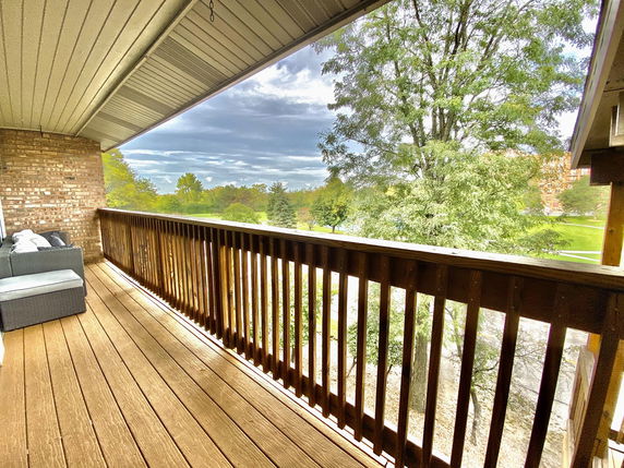 View of surrounding areas from a balcony with wooden railing and seating.