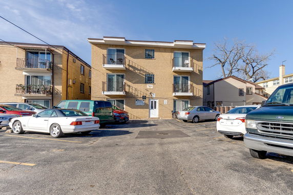 Front view of a multi-story apartment building with balconies and parked cars.