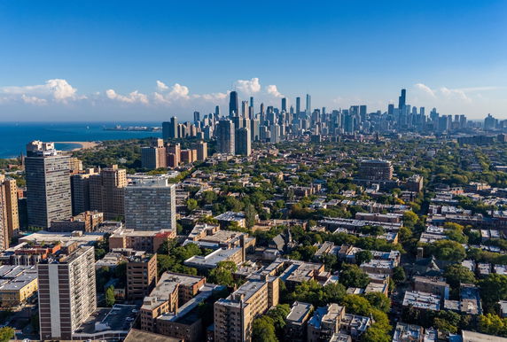Panoramic view of a city skyline with numerous buildings and a large body of water in the background.